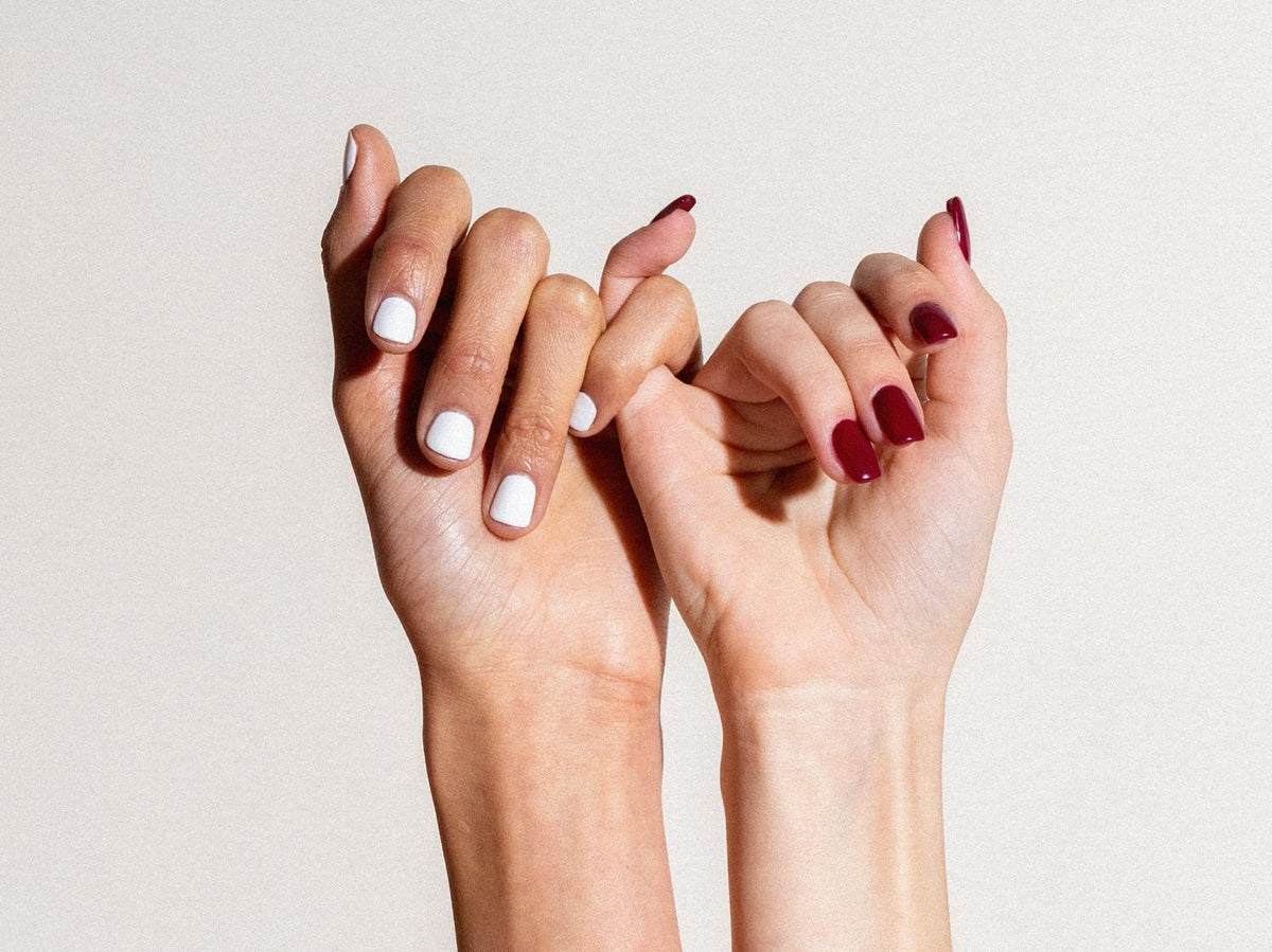 Zwei Hände machen einen kleinen Fingerschwur – eine mit weißen, die andere mit dunkelroten Nägeln.